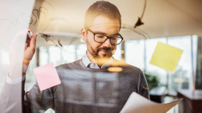 Mann schreibt auf eine Glaswand mit Haftnotizen im modernen Büro.